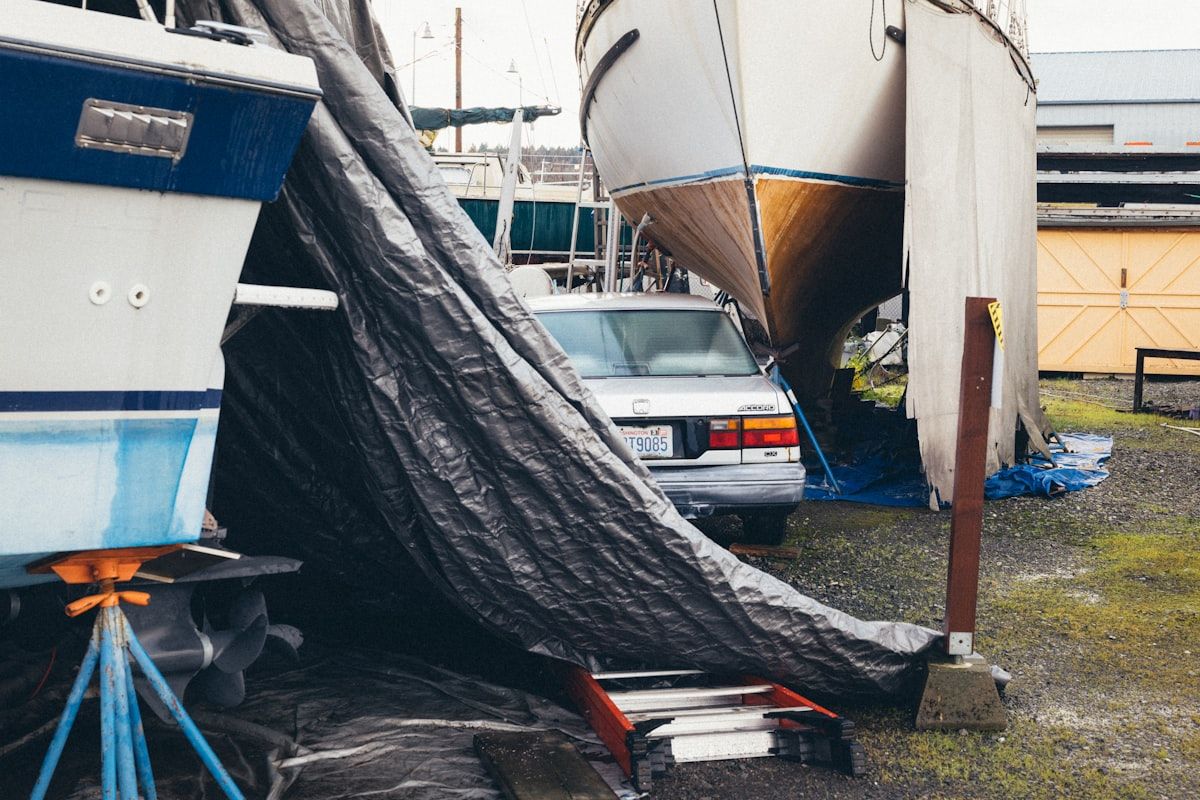 A marine mechanic standing at the stern of a center console boat at a marina slip, inspecting the engine bay with tools laid out on the dock, a tow line coiled nearby, and the boat sitting in calm water under bright afternoon light